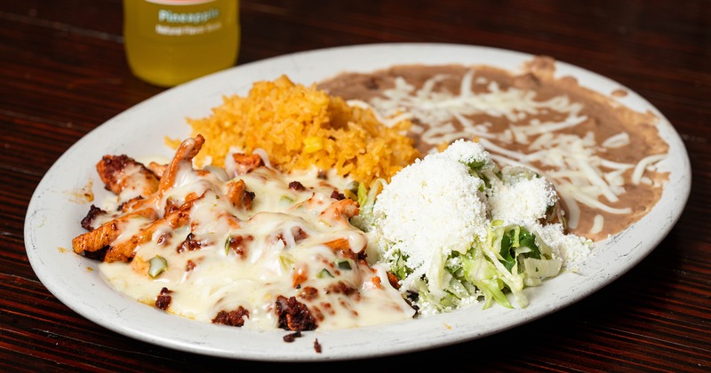 A plate with grilled chicken topped with melted cheese, accompanied with sides and a soft drink
