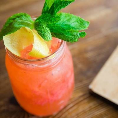 Pink craft cocktail with a lime peel and a mint sprig.