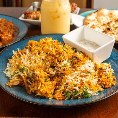 Chicken biryani with a condiment on a blue plate, surrounded by assorted dishes.