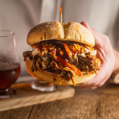 Hands holding a barbecue pulled pork sandwich topped with coleslaw.