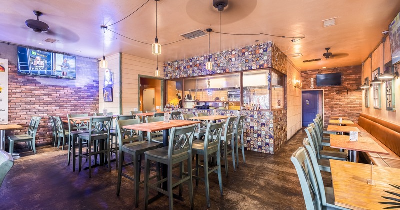 Interior of a cozy Mexican restaurant with an open kitchen, wooden tables, stools, and booth seating