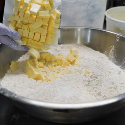 A hand in a purple glove adding cubed butter into a large bowl of flour.