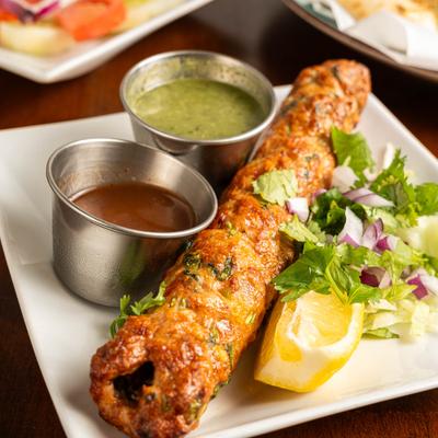 Chicken Seekh Kabab served with chutneys, fresh cilantro, onion, and lemon wedge.