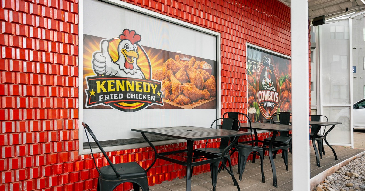 Outdoor seating area with black metal tables and chairs against a vibrant red-tiled wall
