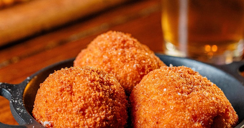 Close up of Mac and Cheese balls in a black dish, set on a wooden table