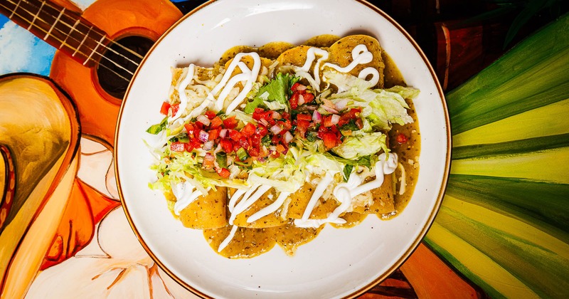 Tortilla chips in smothered in green salsa, with salsa, lettuce, and sour cream
