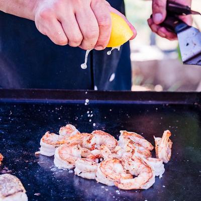 A hand squeezing lemon juice onto shrimp on a grill.