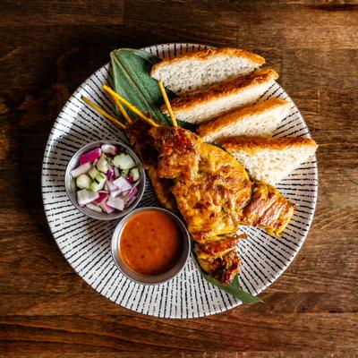 Grilled marinated pork skewers served with bread, dipping sauce, and chopped onions.