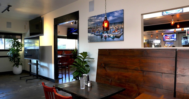 Interior with a wooden booth, table, red chairs, potted plant and a marina photograph on the wall
