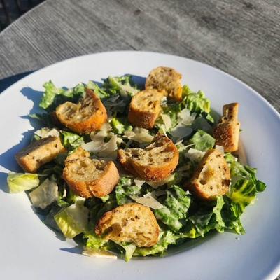 Caesar salad with croutons and Parmesan served on a sunlit outdoor table.