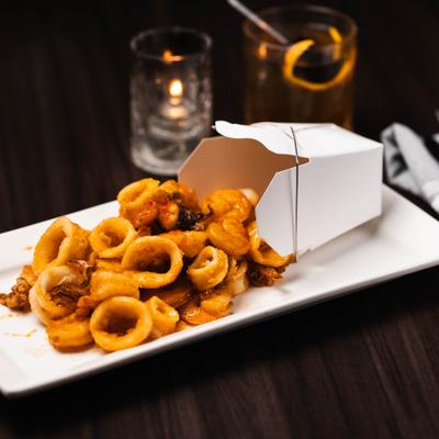 Fried calamari and shrimp in a white takeout container, placed on a rectangular plate.
