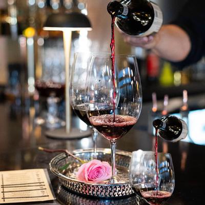 Hand pouring red vine from a bottle into a vine glass.
