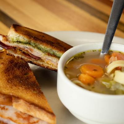 Turkey Pesto Melt sandwich served with a bowl of chicken noodle soup.