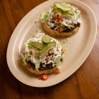 Thick fried corn masa cakes topped with beans, lettuce, crema, and avocado.