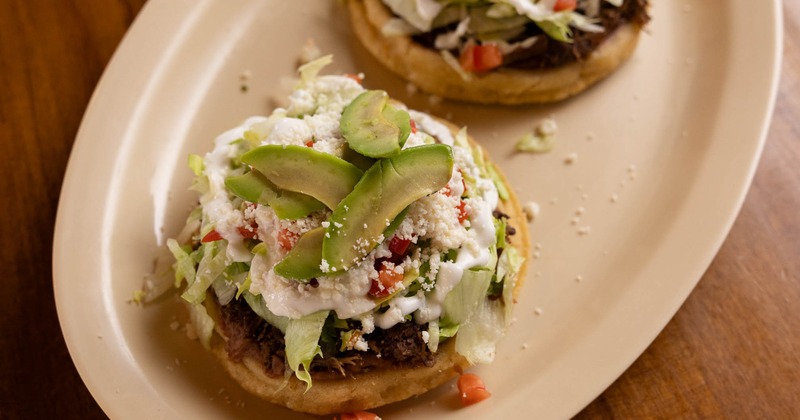 Mexican sopes topped with beans, lettuce, crema, and avocado slices