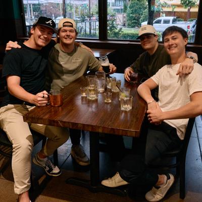 Indoors,  a group of people gathered around a wooden table with drinks.