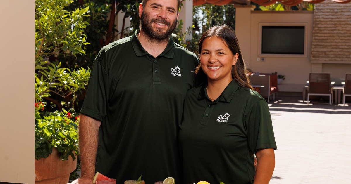 Two people in matching t-shirts posing together on a sunlit restaurant patio