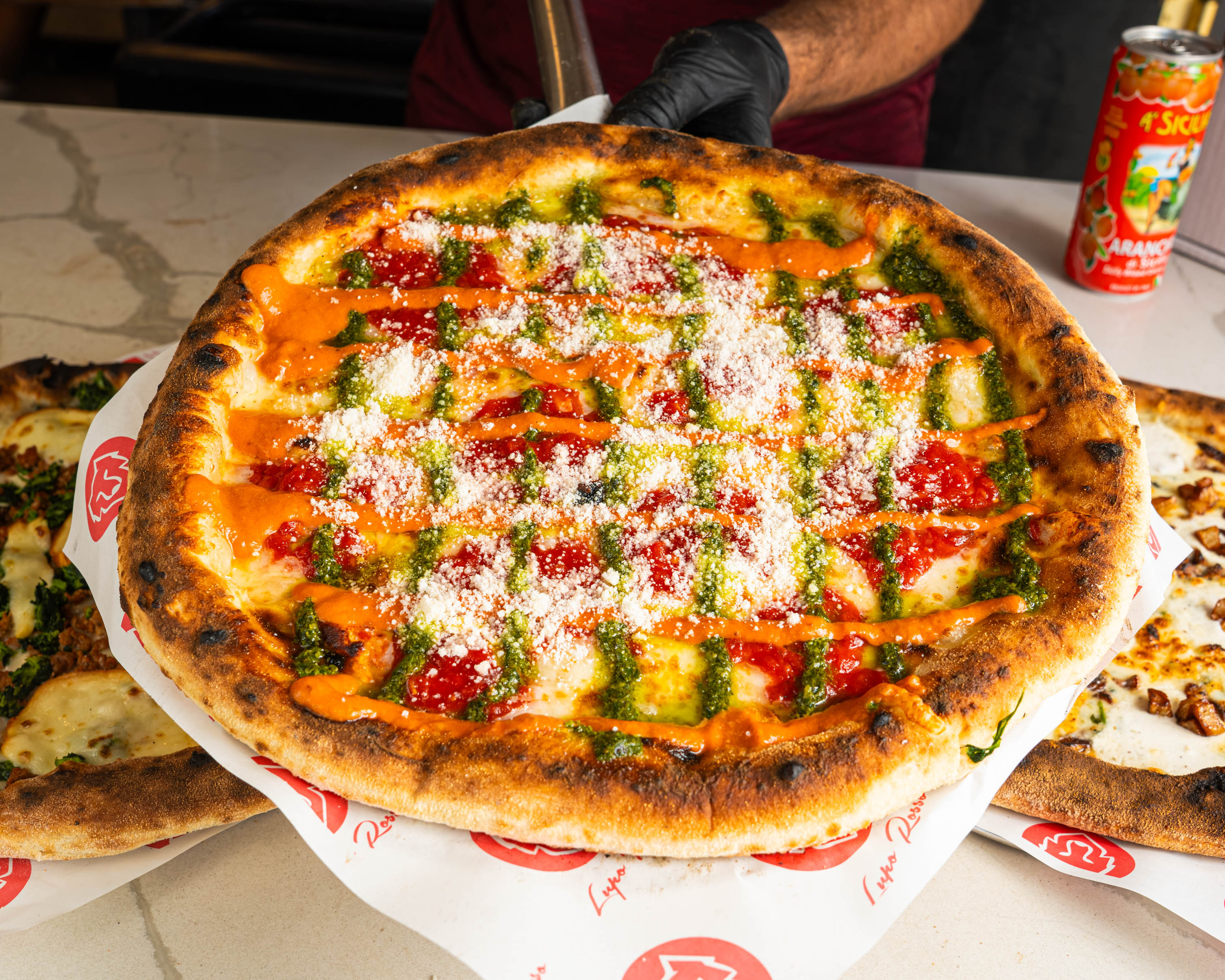 Freshly baked pizza with pesto, marinara sauce, vodka sauce, and grated cheese