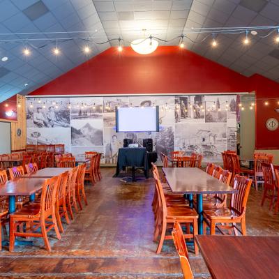 Dining hall with wooden tables, red chairs, and a projector setup.