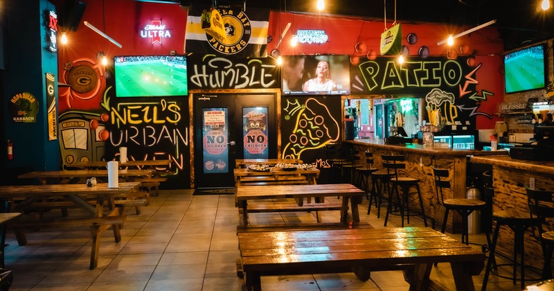 Interior of a lively bar with graffiti, wooden tables, and multiple TVs displaying sports