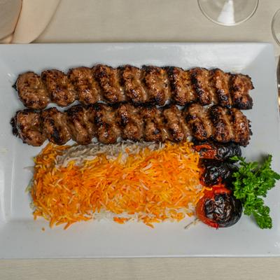Beef kebab with saffron rice and roasted tomatoes on a white rectangular plate.