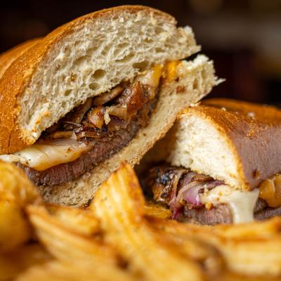 Close up of a steak sandwich served with a side of fries.