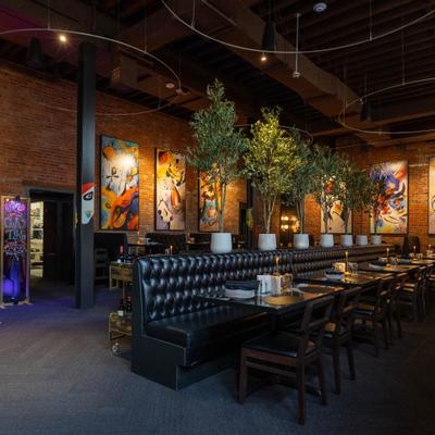 Interior with black banquettes, abstract artwork, potted trees, and warm lighting.
