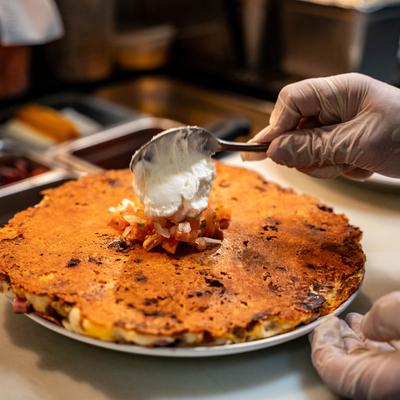 Veggie savory griddle cake, kitchen staff member topping it with sour cream.