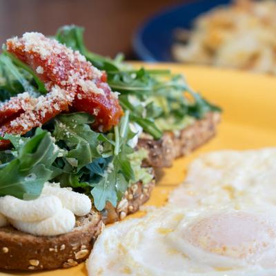Avocado toast, with arugula, tomato, parmesan, ricotta, and fried eggs.