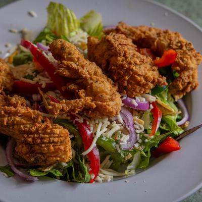 Fried chicken strips served over garden salad on plate.