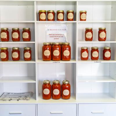 Jars of  signature marinara arranged on white shelves.