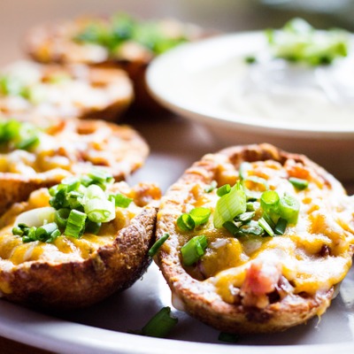Potato skins topped with cheese and green onion plated with a side of sour cream