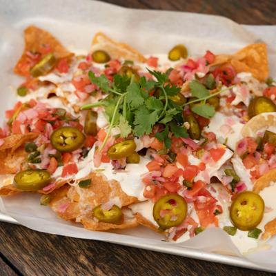 Nachos topped with a white queso sauce, pico de gallo, pickled jalapeños and cilantro.