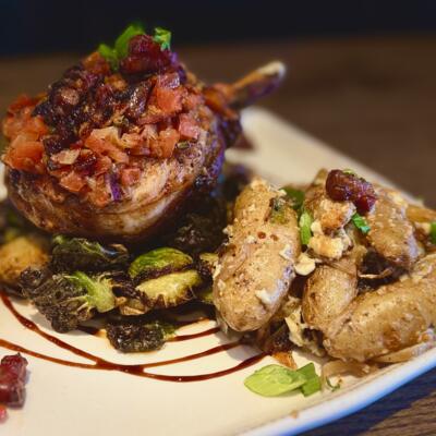 Pork chop topped with bacon and tomatoes, served with brussels sprouts and roasted potatoes.