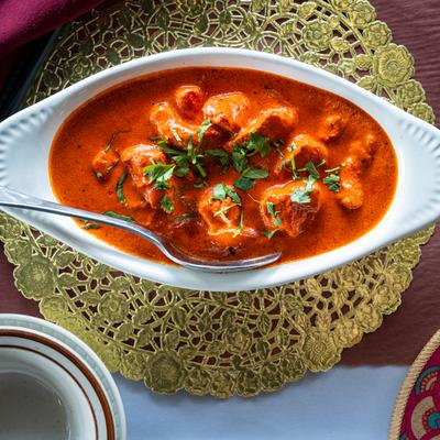 Chicken tikka masala in a white oval dish, garnished with cilantro, served on a gold lace placemat.