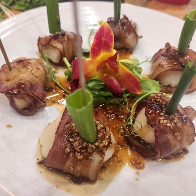 Bacon-wrapped scallops with sesame glaze and edible flowers.