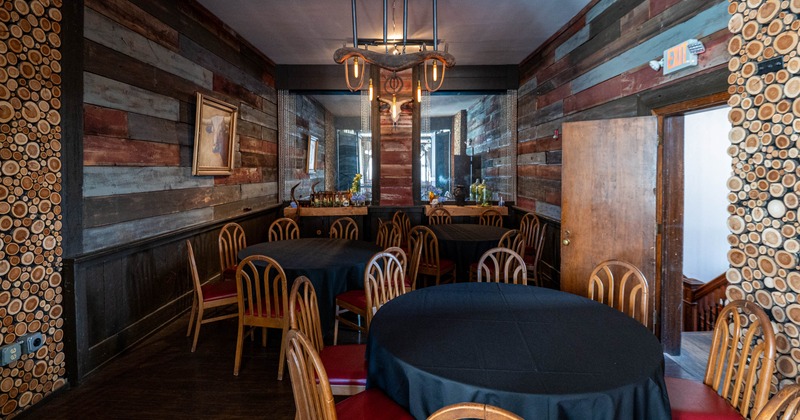 Rustic dining room, wooden walls, round tables with black tablecloths and wooden chairs