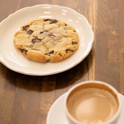 A chocolate chip cookie served on a plate next to a cup of coffee.