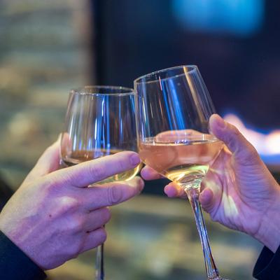 Two people clink glasses filled with white wine in a toast.