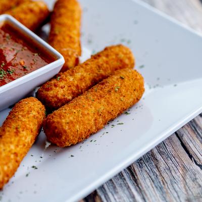 Close up shot of mozzarella sticks on the plate with marinara sauce.