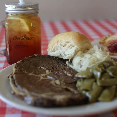 Ribeye steak served with green beans, mashed potatoes, and a bun, accompanied with iced tea.