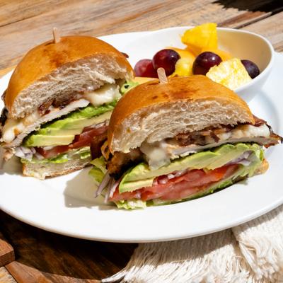 Chicken and avocado club sandwich on a bun served with mixed fruit.