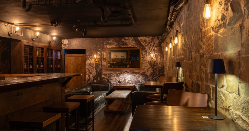 Cozy, dimly lit bar with rustic stone walls, leather couches, wooden tables