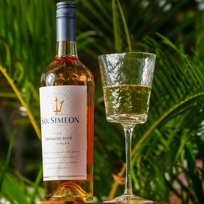 San Simeon rosé, bottle and glass resting in front of palm branches.