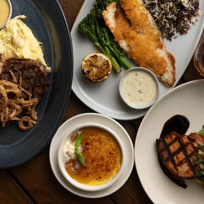 Dinner spread with steak, breaded fish, grilled pork chop, and creme brulee.