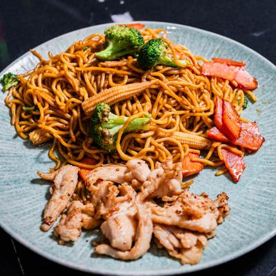 Stir fried noodles with vegetables and sliced chicken on plate.