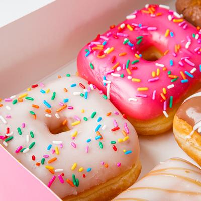A close-up of colorful assorted donuts with sprinkles in a pink box.