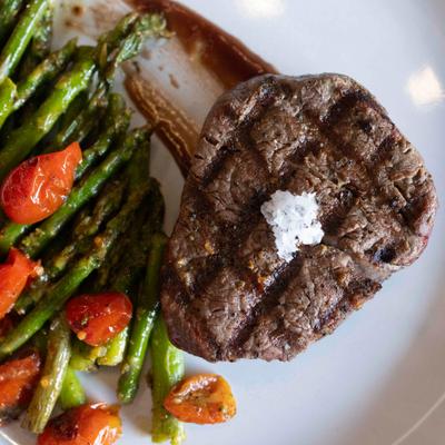Grilled steak topped with coarse salt served alongside asparagus and roasted cherry tomatoes.