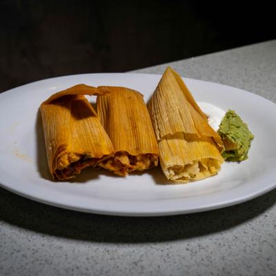 Tamales served with guacamole and sour cream on a white plate.