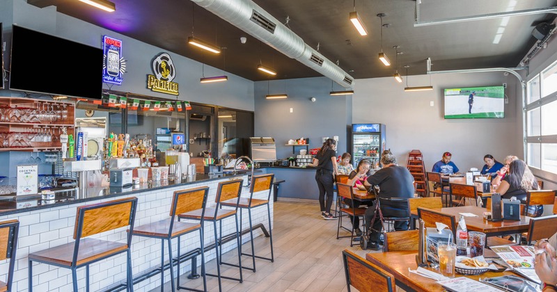 Interior, bar with chairs, people at tables dining, staff member taking an order